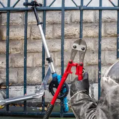 Un individu masqué, ganté, s'apprête à couper le cadenas d'une trottinette électrique avec une pince monstre.