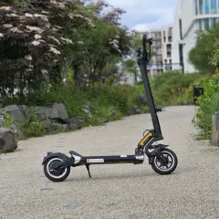 Trottinette électrique Dualtron Togo noire, sur un chemin pavé, avec des rochers et de la végétation.