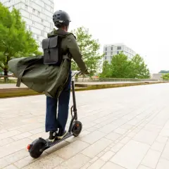 Personne casquée sur trottinette électrique, manteau long flottant, pour augmenter l'autonomie de sa trottinette électrique en ville.
