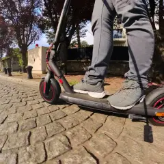 Pieds sur un trottinette pro 4 Xiaomi, roulant sur une rue pavée bordée d'arbres et de maisons.