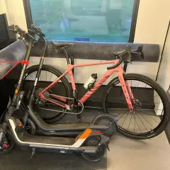 Une trottinette et un vélo rose sont rangés dans un compartiment de train, prêts pour l'aventure.
