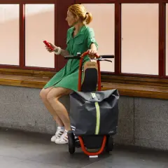 Femme en robe verte assise, tenant un téléphone rouge, à côté d'une trolley trottinette grise et orange.