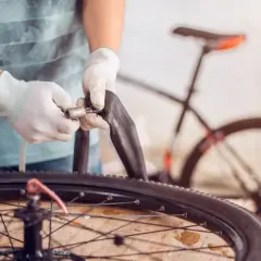 Mains gantées manipulant une chambre à air pour changer celle de la roue arrière d'un vélo électrique.