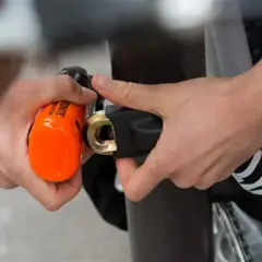 Mains sécurisant un vélo avec un antivol alarme orange vif. Le cadenas est solidement attaché au cadre.