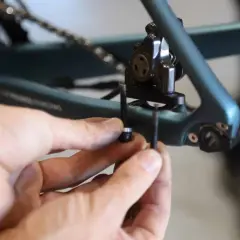 Mains ajustant la vis du frein à disque 140mm sur un cadre de vélo bleu.