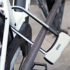 Un antivol pour vélo avec alarme intégrée protège un vélo blanc. Le cadenas en U est fixé au cadre et à la roue arrière.