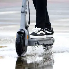 Trottinette électrique en action, éclaboussant l'eau sous la pluie. La protection ip54 assure une résistance à l'eau pour continuer le trajet.