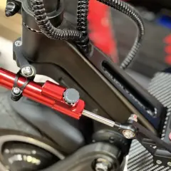 Amortisseur de direction trottinette rouge vif, fixé sur le châssis noir, prêt à améliorer la stabilité.