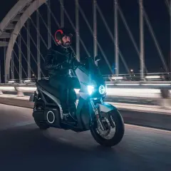 Un homme roule en scooter électrique sur un pont la nuit, profitant de la récupération d'énergie pour prolonger son trajet.