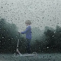 Un enfant sur une trottinette, sous la pluie. Le **signification IP54** protège de la poussière et des éclaboussures.