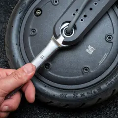 Main tenant utilise une clé pour changer la roue avant d'une trottinette électrique.