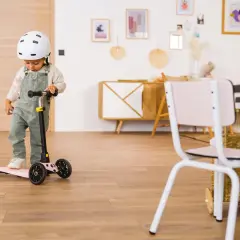 Un enfant porte un casque et se tient sur une trottinette rose. Il semble prêt à explorer, peut-être avec des stickers trottinette personnalisés pour ajouter une touche de couleur.