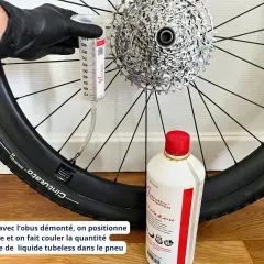 Maintenant, découvrez comment mettre liquide préventif tubeless : une seringue injecte le produit dans le pneu de vélo, à côté d'une bouteille de liquide.
