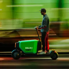 Un livreur sur une trottinette cargo verte "DELIVERY" file dans la nuit, le paysage flou derrière lui.