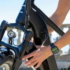 Main d'une personne âgée insérant la clé dans le cadre d'un vélo électrique. La montre connectée affiche "End Workout".