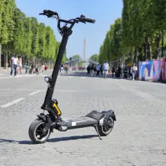 Trottinette électrique Dualtron Togo Plus sur une avenue bordée d'arbres, avec des passants et des décorations colorées en arrière-plan.