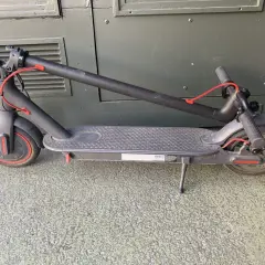 Trottinette électrique noire pliée, avec un câble rouge visible. Un kit d'étanchéité pour trottinette électrique pourrait être utile pour la protéger.