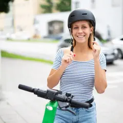 Jeune femme souriante ajustant son casque trottinette électrique, prête pour une balade en ville.