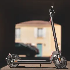 Trottinette électrique Wispeed T850 noire, vue de profil, devant une maison floue.
