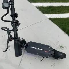 Trottinette électrique Dualtron Victor, noire, sur un sol en dalles de béton et herbe. Le poids de ce modèle est un atout pour sa maniabilité.