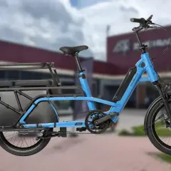 Vélo longtail bleu électrique, idéal pour transporter des passagers ou des courses grâce à sa longue plateforme arrière et ses sièges.