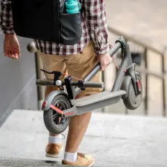 Un homme porte sa trottinette électrique pliée, peut-être pour la vendre ou la transporter.