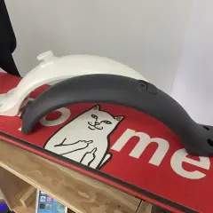 Deux garde boue trottinette Xiaomi, un blanc et un noir, posés sur un deck rouge orné d'un chat.