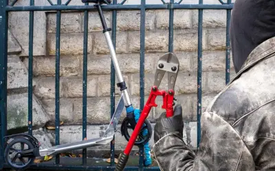 Un individu masqué, ganté, s'apprête à couper le cadenas d'une trottinette électrique avec une pince monstre.