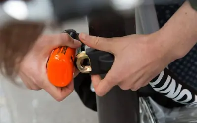 Mains sécurisant un vélo avec un antivol alarme orange vif. Le cadenas est solidement attaché au cadre.