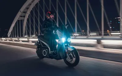 Un homme roule en scooter électrique sur un pont la nuit, profitant de la récupération d'énergie pour prolonger son trajet.