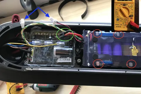 Comment tester une batterie de trottinette : un multimètre jaune affiche 00.1V, des fils connectés à une carte mère et une batterie.