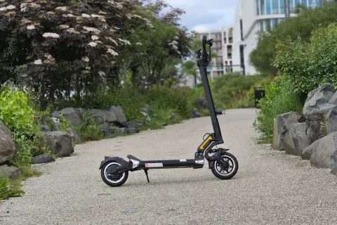 Trottinette électrique Dualtron Togo noire, sur un chemin pavé, avec des rochers et de la végétation.