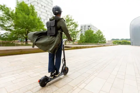 Personne casquée sur trottinette électrique, manteau long flottant, pour augmenter l'autonomie de sa trottinette électrique en ville.