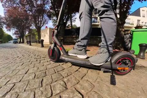 Pieds sur un trottinette pro 4 Xiaomi, roulant sur une rue pavée bordée d'arbres et de maisons.
