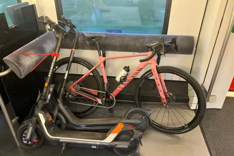 Une trottinette et un vélo rose sont rangés dans un compartiment de train, prêts pour l'aventure.
