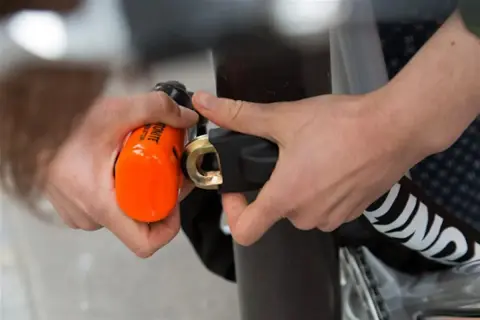 Mains sécurisant un vélo avec un antivol alarme orange vif. Le cadenas est solidement attaché au cadre.