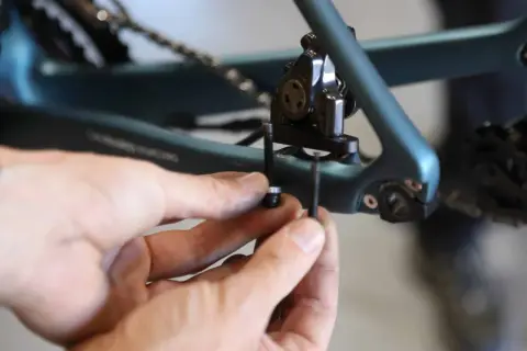 Mains ajustant la vis du frein à disque 140mm sur un cadre de vélo bleu.