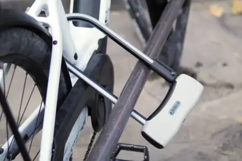 Un antivol pour vélo avec alarme intégrée protège un vélo blanc. Le cadenas en U est fixé au cadre et à la roue arrière.