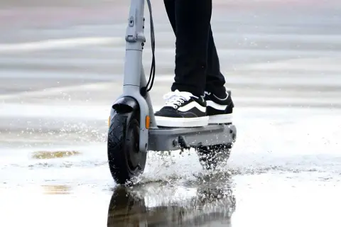 Trottinette électrique en action, éclaboussant l'eau sous la pluie. La protection ip54 assure une résistance à l'eau pour continuer le trajet.