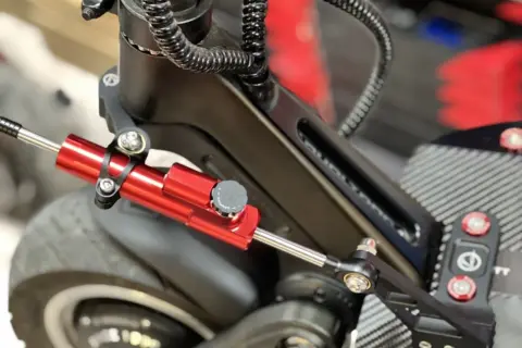 Amortisseur de direction trottinette rouge vif, fixé sur le châssis noir, prêt à améliorer la stabilité.