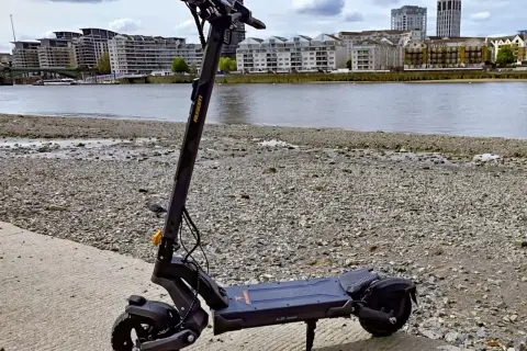 Trottinette électrique noire posée sur un chemin de gravier, avec une rivière et des immeubles en arrière-plan. Idéal pour savoir où garer sa trottinette électrique.