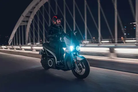 Un homme roule en scooter électrique sur un pont la nuit, profitant de la récupération d'énergie pour prolonger son trajet.
