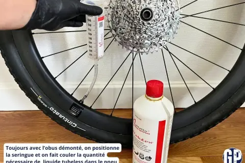 Maintenant, découvrez comment mettre liquide préventif tubeless : une seringue injecte le produit dans le pneu de vélo, à côté d'une bouteille de liquide.