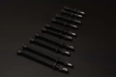 Plusieurs valves Schrader noires, alignées sur un fond sombre, prêtes pour une nouvelle aventure cycliste.