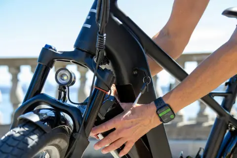 Main d'une personne âgée insérant la clé dans le cadre d'un vélo électrique. La montre connectée affiche "End Workout".