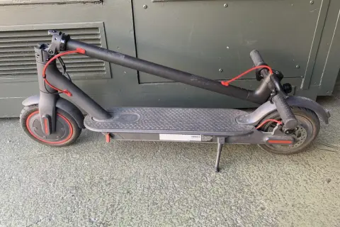 Trottinette électrique noire pliée, avec un câble rouge visible. Un kit d'étanchéité pour trottinette électrique pourrait être utile pour la protéger.
