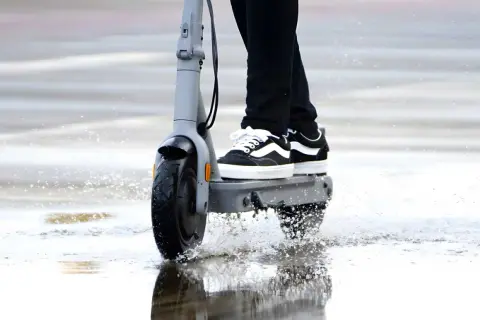 Une trottinette électrique roule dans une flaque d'eau, soulevant des éclaboussures. La question est : peut-on rouler sous la pluie avec une trottinette électrique ?