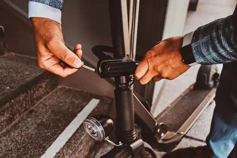Un homme utilise une clé pour activer l'antivol de sa trottinette électrique, assurant ainsi sa sécurité.