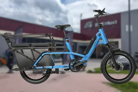 Vélo longtail bleu électrique, idéal pour transporter des passagers ou des courses grâce à sa longue plateforme arrière et ses sièges.