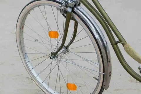 Roue de vélo verte avec garde-boue chromé et deux catadioptres orange pour la sécurité.